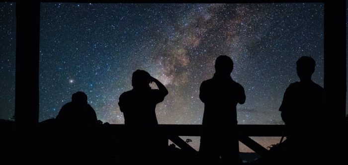 Four people stargazing silhouetted against the milky way